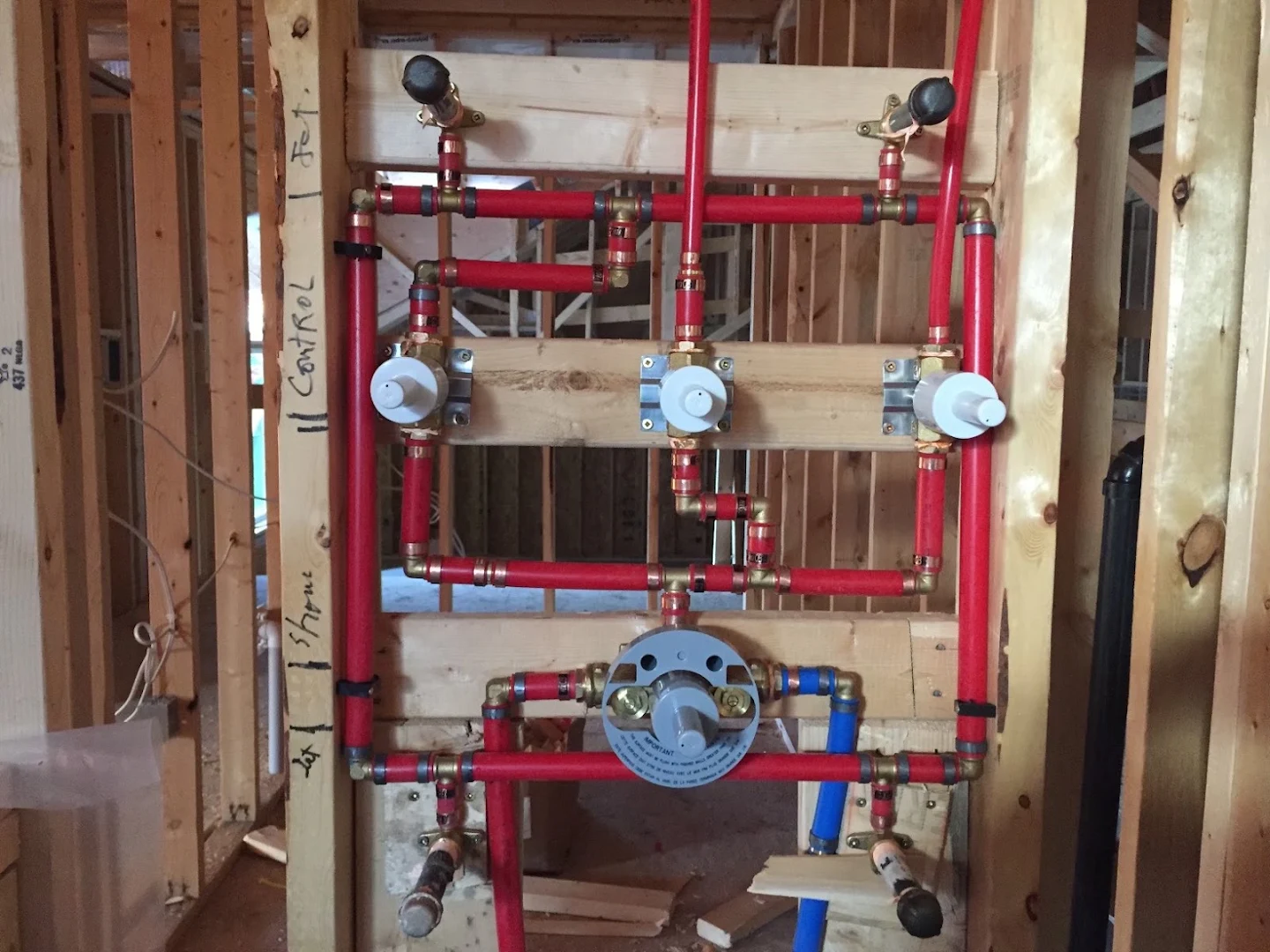Red water supply piping and shower valve rough-in installed between exposed wall studs by Apex Plumbing