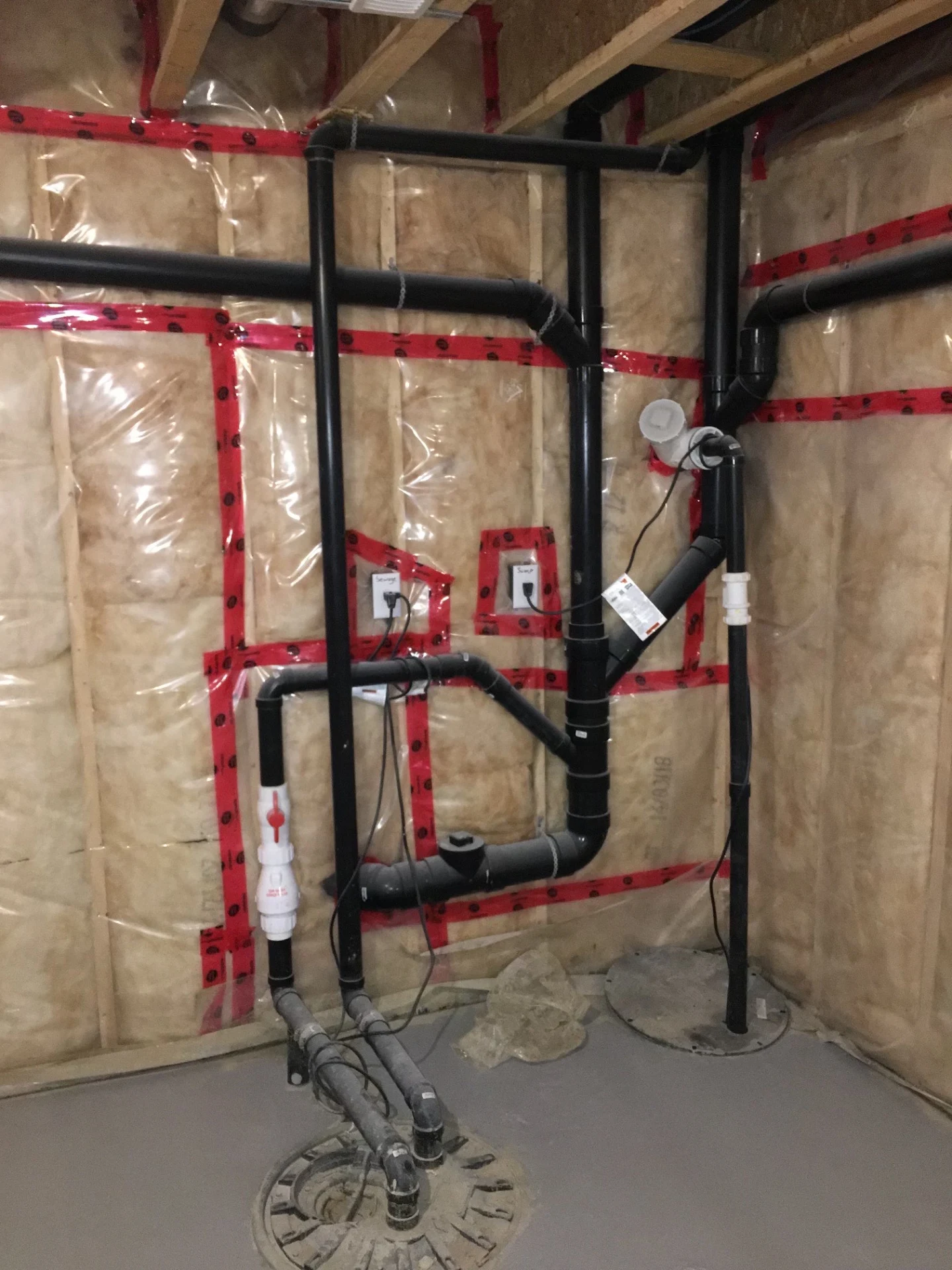 Basement sump and drainage plumbing with black drain lines installed by Apex Plumbing